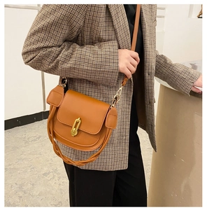 Dettaglio borsa a sella in pelle caramello con fibbia dorata e finiture intrecciate alla moda
