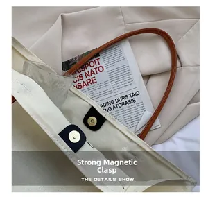 Dettaglio della chiusura magnetica su borsa tote in tela crema con manici in pelle marrone