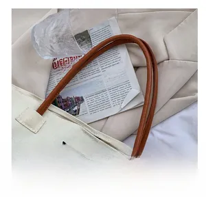 Dettaglio borsa shopper in tela beige con manici in pelle marrone ed etichetta nera