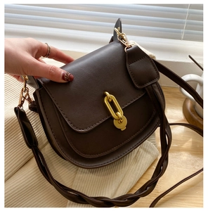 Dettaglio borsa a sella marrone con fibbia dorata e tracolla intrecciata stile vintage