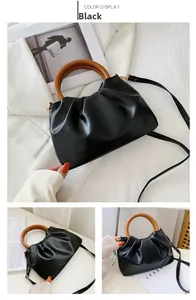 Detail of black pleated cloud bag with round wooden handle and slim crossbody strap