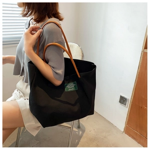 Borsa tote in tela nera con manici in pelle marrone indossata sulla spalla