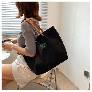Dettaglio di una borsa tote in tela nera con manici in pelle indossata da una modella