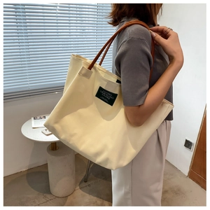 Dettaglio di una grande borsa tote in tela crema con manici marroni ed etichetta nera