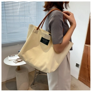 Dettaglio di una borsa tote in tela con manici in pelle marrone ed etichetta nera