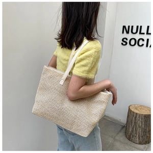 Close-up of beige woven tote bag featuring white leather handles and detailed texture