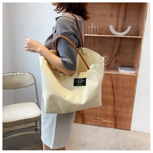 Dettaglio della borsa tote in tela crema con manici in pelle marrone ed etichetta verde