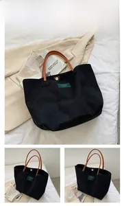 Dettaglio della borsa tote in tela nera con manici in pelle marrone ed etichetta del marchio