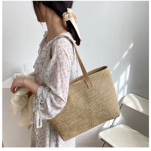 Close-up of woven straw tote bag with brown faux leather handles and detailed texture