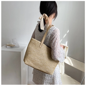 Detail of woven straw tote bag texture and brown leather shoulder strap on a female model