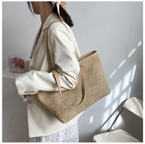 Detail of woven straw tote bag with brown leather shoulder straps worn by a model