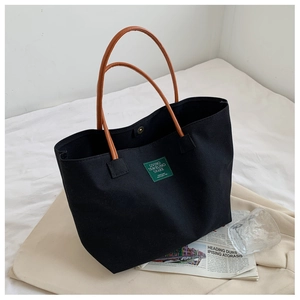 Detail of black canvas tote bag featuring brown leather handles and green textile patch label