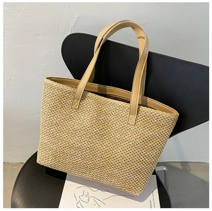 Detail of hand-woven straw tote bag with brown faux leather handles on a black chair