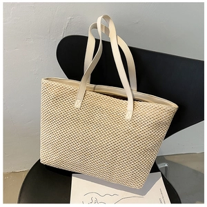 Detail of beige woven straw tote bag texture and cream PU leather handles on a chair