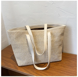 Detail of woven straw tote bag with premium leather handles on a wooden surface