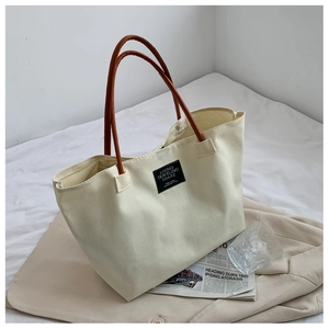 Detail of minimalist off-white canvas tote bag featuring brown leather handles and chic label