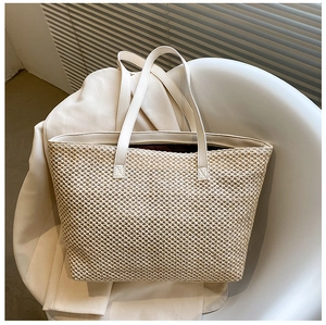 Detail of hand-woven straw tote bag with cream leather handles and woven texture