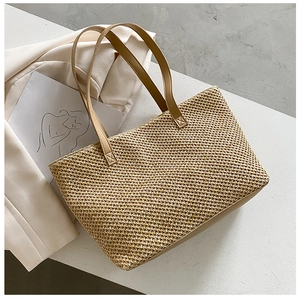 Top view of a woven straw tote bag with brown leather handles on a white blazer background