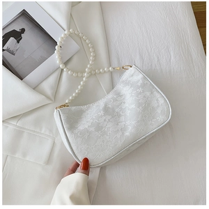 Detailed close-up of white floral lace handbag with elegant pearl handle on a white blazer