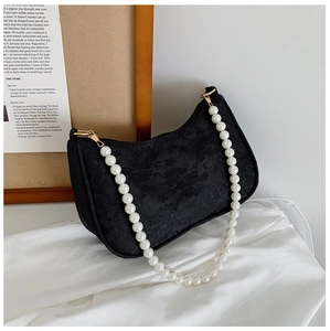 Detail of black lace baguette bag with floral texture and white pearl chain strap