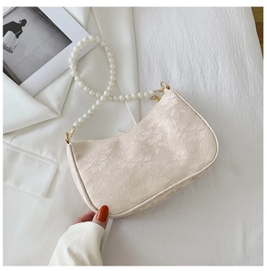 Close-up of the delicate floral lace texture and elegant pearl handle on the cream baguette bag