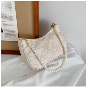 Close-up of cream lace texture on baguette bag with elegant pearl chain and gold zipper