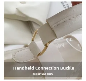 Detail of the golden D-ring hardware and leather handle stitching on a beige handbag