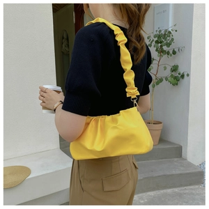 Detail of yellow pleated cloud bag with scrunchie strap in outdoor lifestyle setting