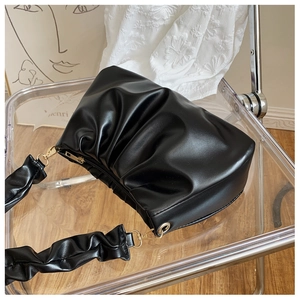 Detail of black pleated cloud bag with golden zipper on a modern minimalist chair