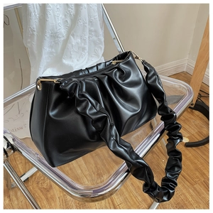 Detail of black pleated cloud bag with glossy texture and golden metallic buckle