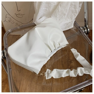 Close-up of a white pleated cloud bag with a matching shoulder strap on a modern chair