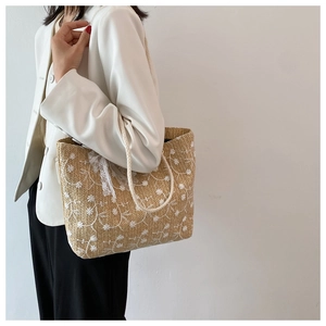 Detail der Strohtasche mit Gänseblümchen-Stickerei und weißer Spitzenschleife