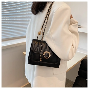 Detail of black quilted leather crossbody bag with pearl buckle and metal chain strap