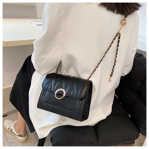 Model wearing a black quilted crossbody bag with gold chain and pearl buckle detail