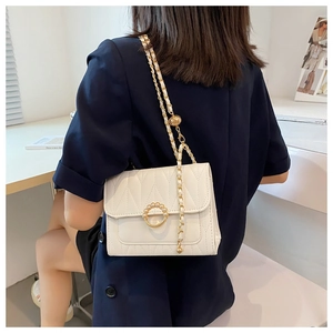 Detail of a beige quilted crossbody bag featuring a pearl-accented metal ring and chain strap