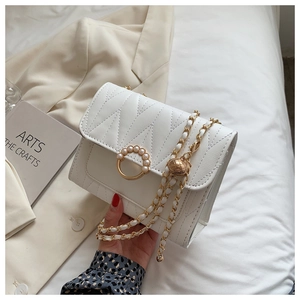 Close-up of white quilted crossbody bag with pearl buckle and gold chain strap detail