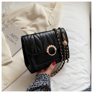 Close-up of quilted black crossbody bag with V-stitches and pearl gold clasp