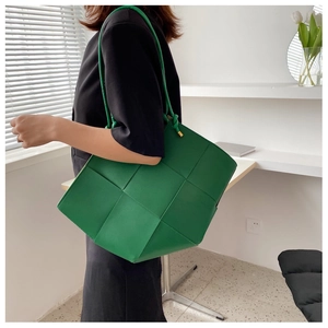 Detail of green woven leather tote bag showing wide Intrecciato pattern and thin handles
