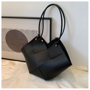 Detailed close-up of a black woven tote bag with large leather strips and gold metal tips