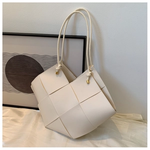 Close-up of beige woven tote bag with knotted leather straps and gold metal tips