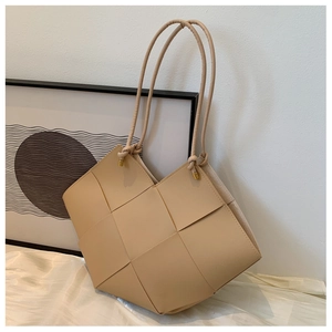 Close-up of beige woven tote bag showing leather strap detail and golden metal hardware