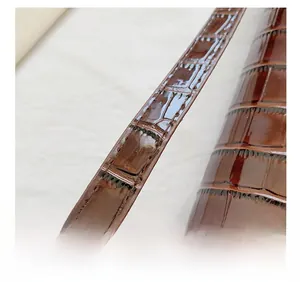 Macro detail of glossy brown crocodile pattern leather shoulder strap and stitching