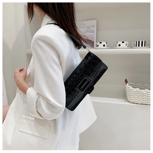 Detail of black crocodile embossed square bag with gold metal buckle on a white blazer