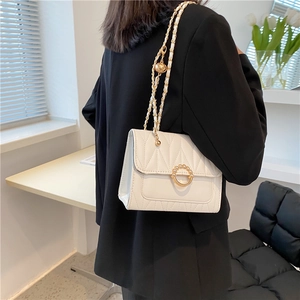 White quilted crossbody bag with gold pearl buckle worn over a black blazer jacket