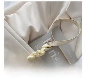 Detail of the woven ribbon strap and smooth leather texture on an off-white shoulder bag
