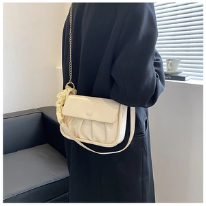 Detail of cream pleated cloud bag with gold chain strap styled on a black blazer