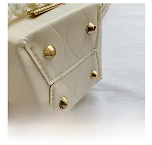 Detail of beige bucket bag base with protective gold studs and pearl handle accent