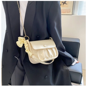 Detail of cream pleated crossbody bag with gold chain and yellow bow charm on model