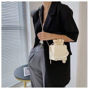 Detail of cream cube bag with pearl handle and drawstring closure on black blazer