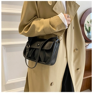 Detail of black pleated cloud bag with snap button flap worn with a stylish trench coat